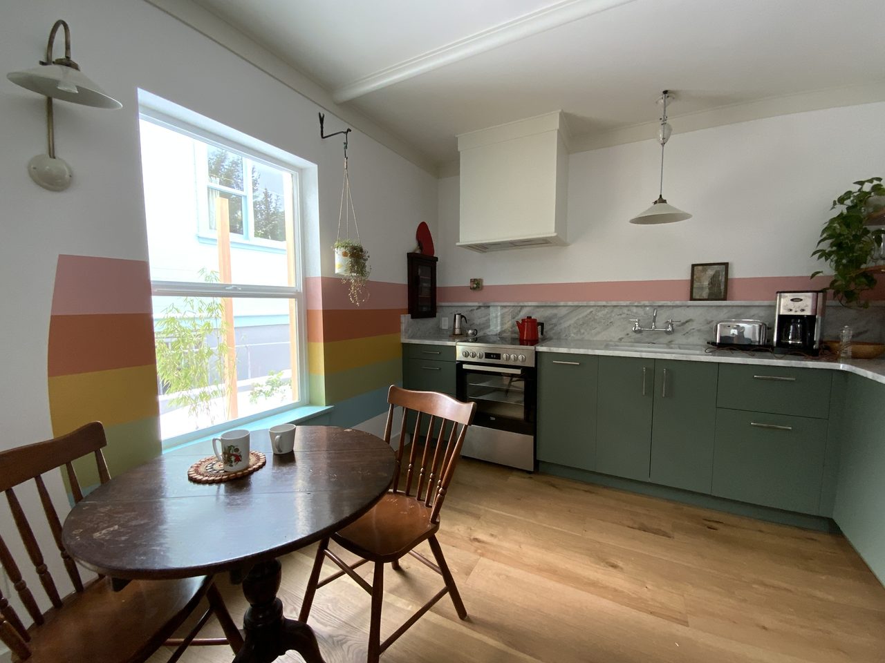Sunny kitchen with a round wooden table, teal cabinets and rainbow-striped walls